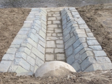 Rekonstrukce odpadního koryta (dlažba z lomového kamene do betonu), odtěžení nánosů z bermy